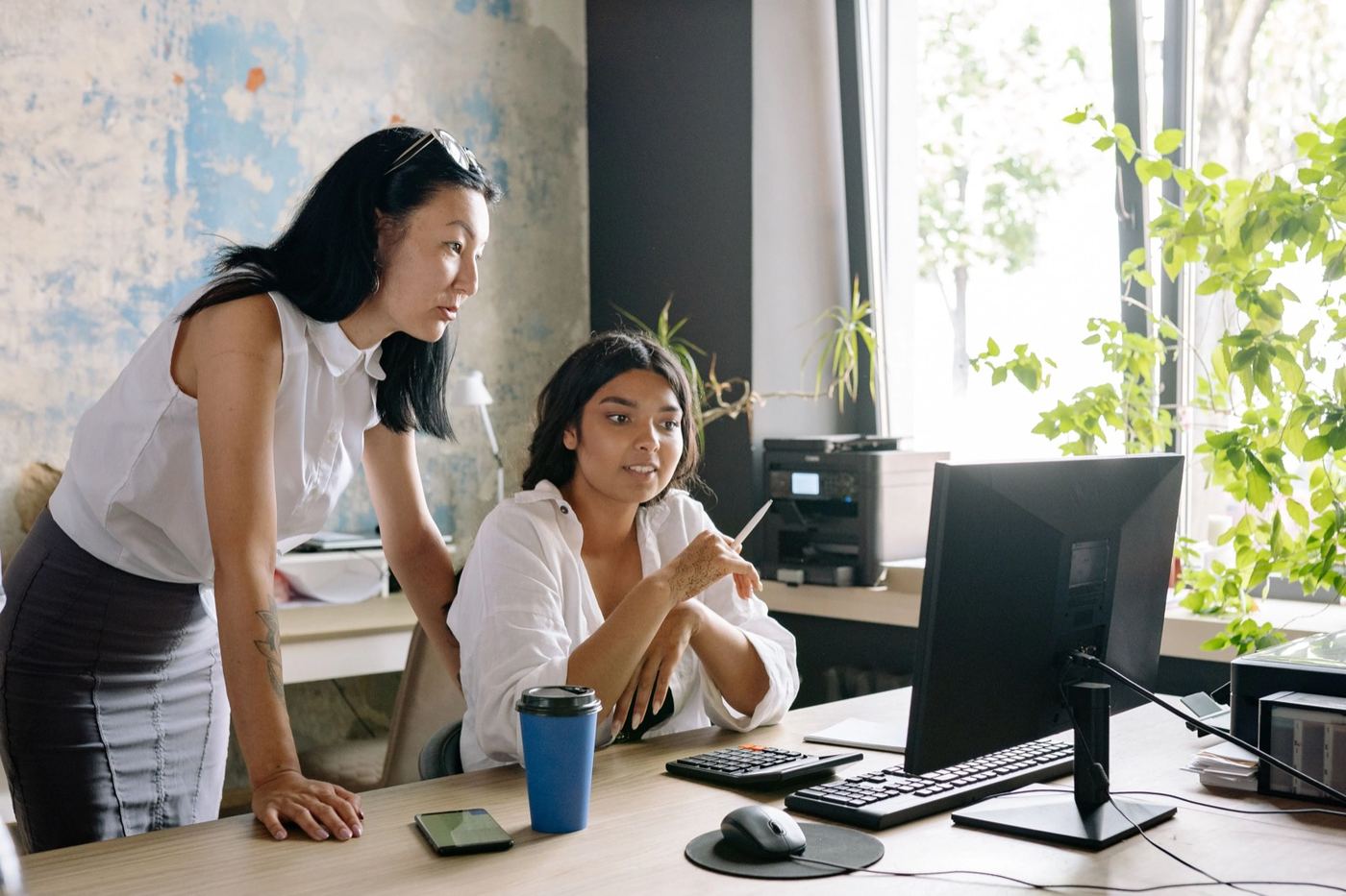 Two colleagues working together at a desk, looking at the same screen