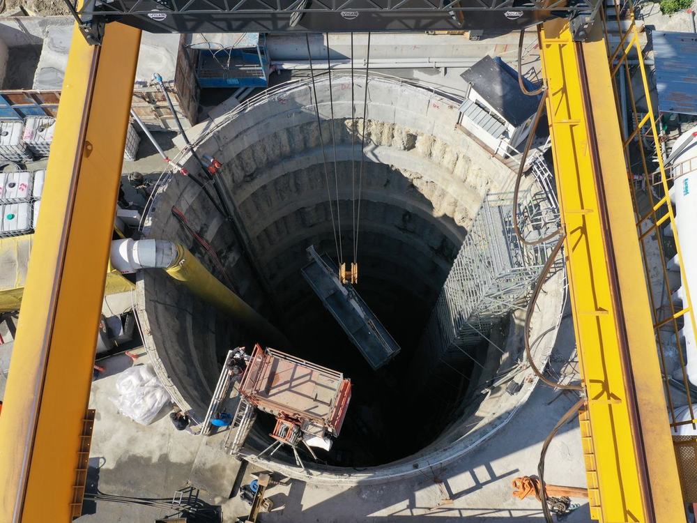 A deep circular shaft under excavation, gantry cranes across its mouth