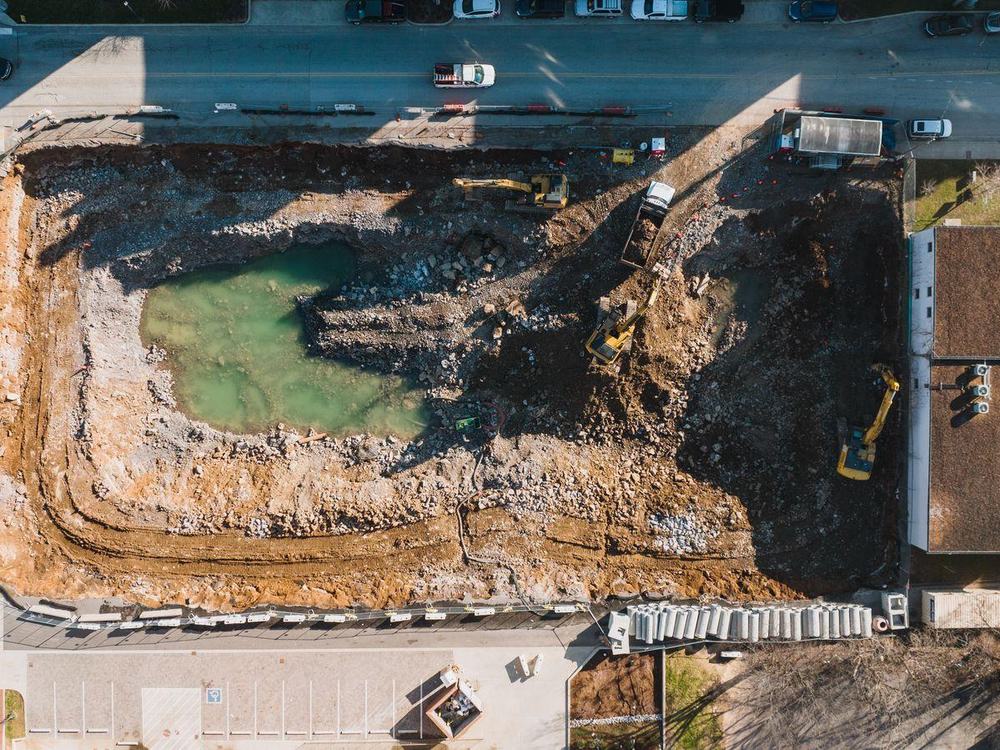 A deep excavation pit beside a road, water pooled at the bottom