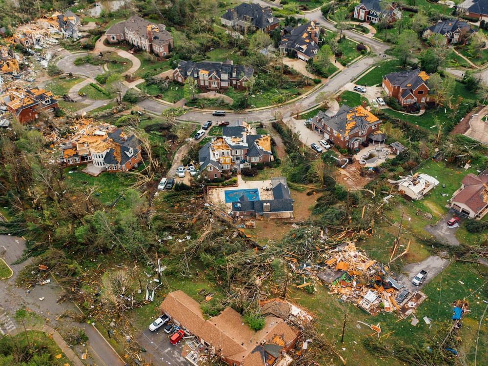 A neighbourhood after a storm, roofs torn away and debris across the gardens