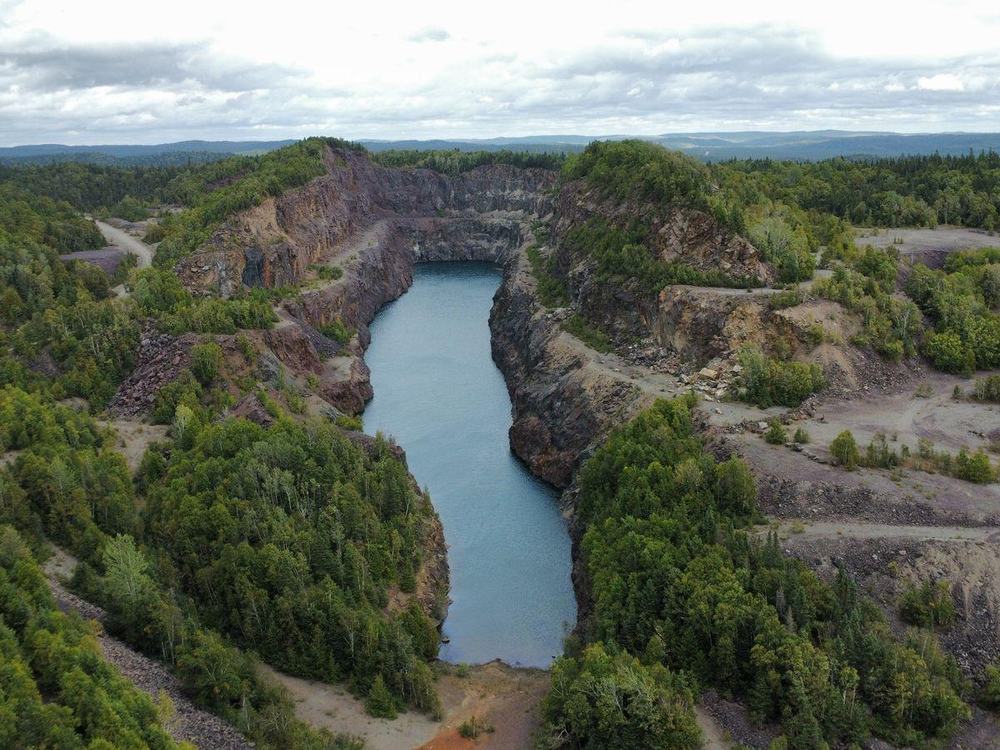 A flooded quarry, still water held between rock walls and regrown trees