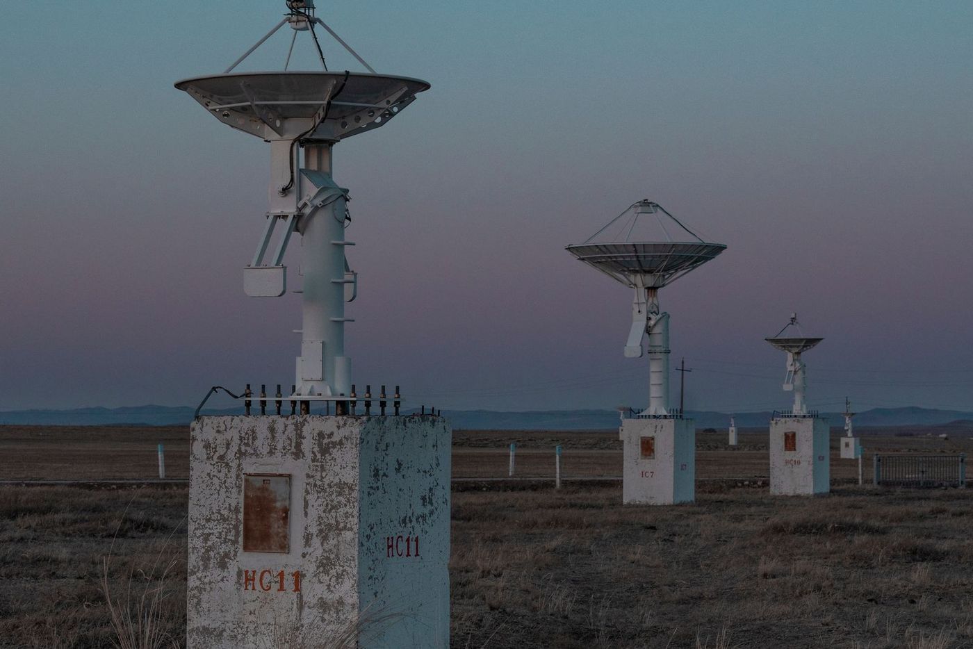Satellite ground-station antennas standing across open ground at dusk