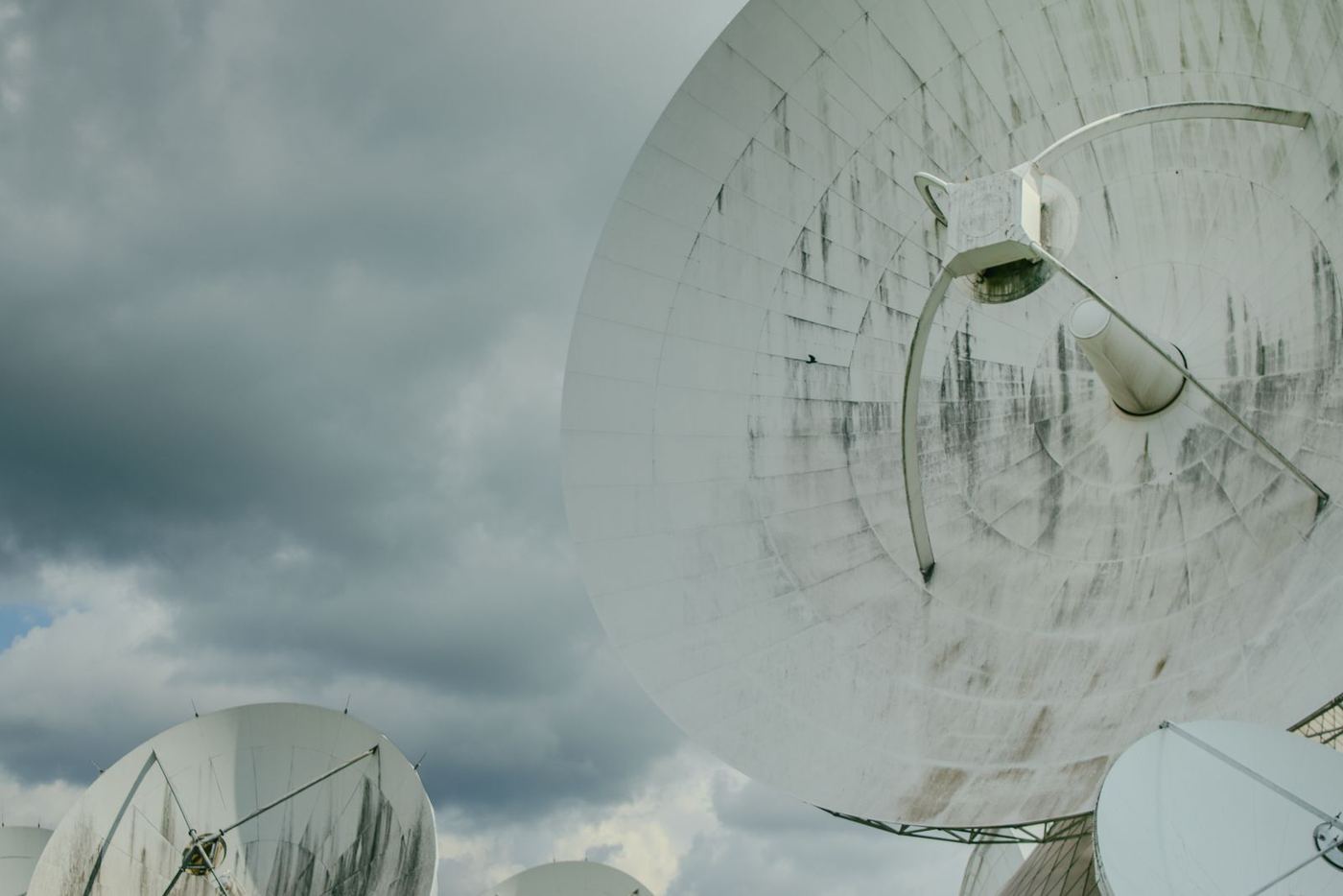 A row of satellite dishes angled at an overcast sky