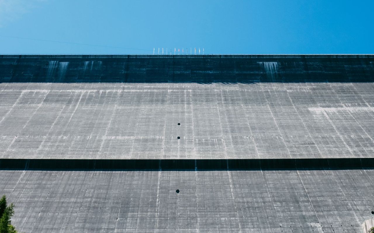 The face of a large concrete dam rising against a clear sky
