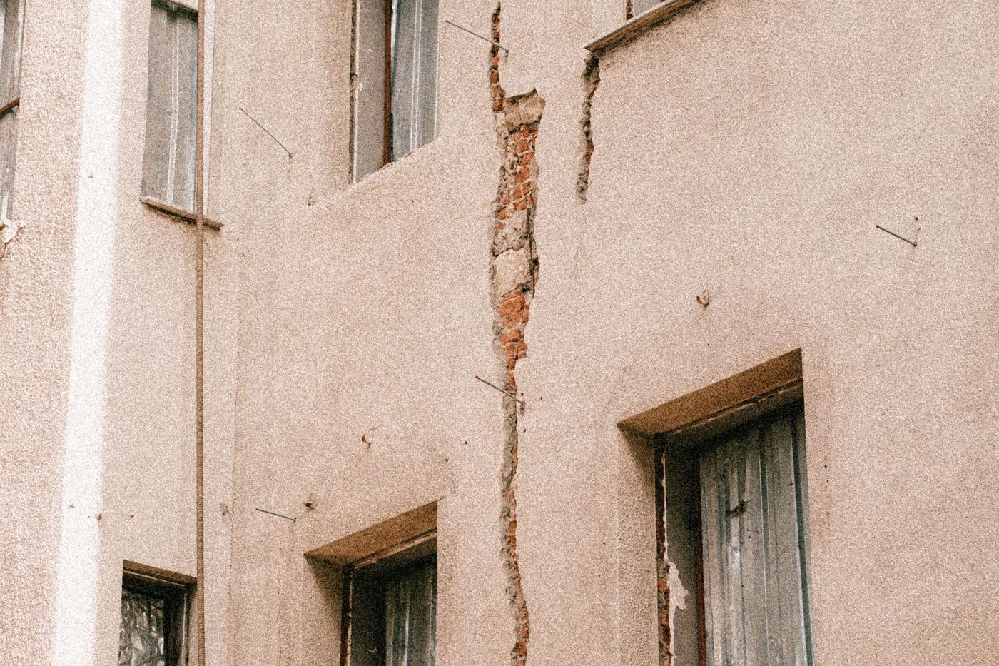 A crack running the full height of a rendered building facade, between the windows