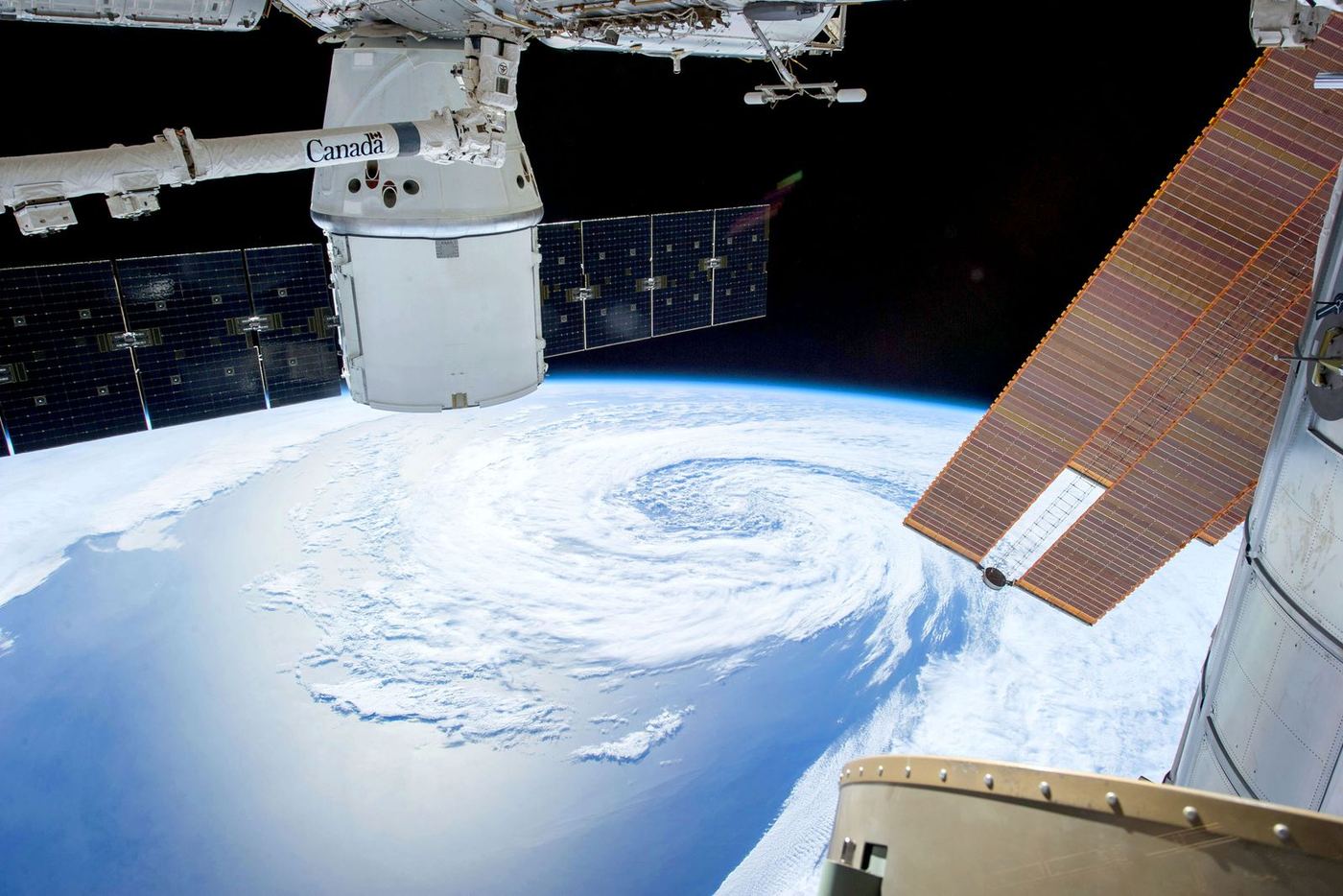 A spacecraft’s solar arrays above a cyclone turning over the ocean
